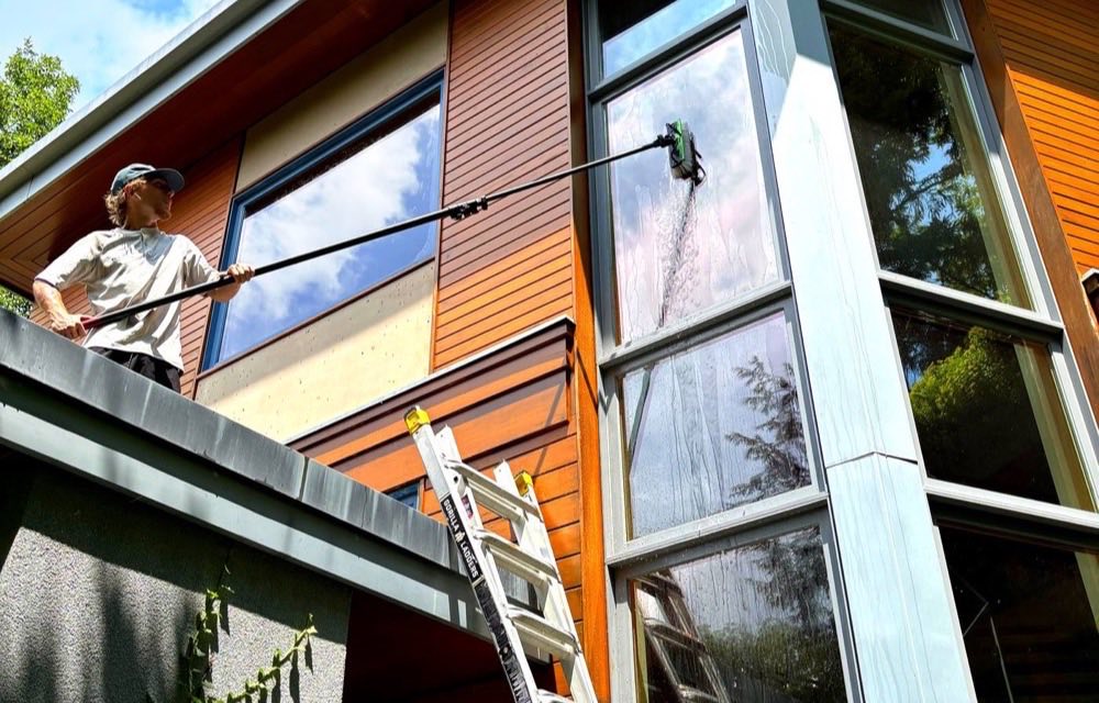 White Diamond Cleaning technician washing upper windows on a modern home